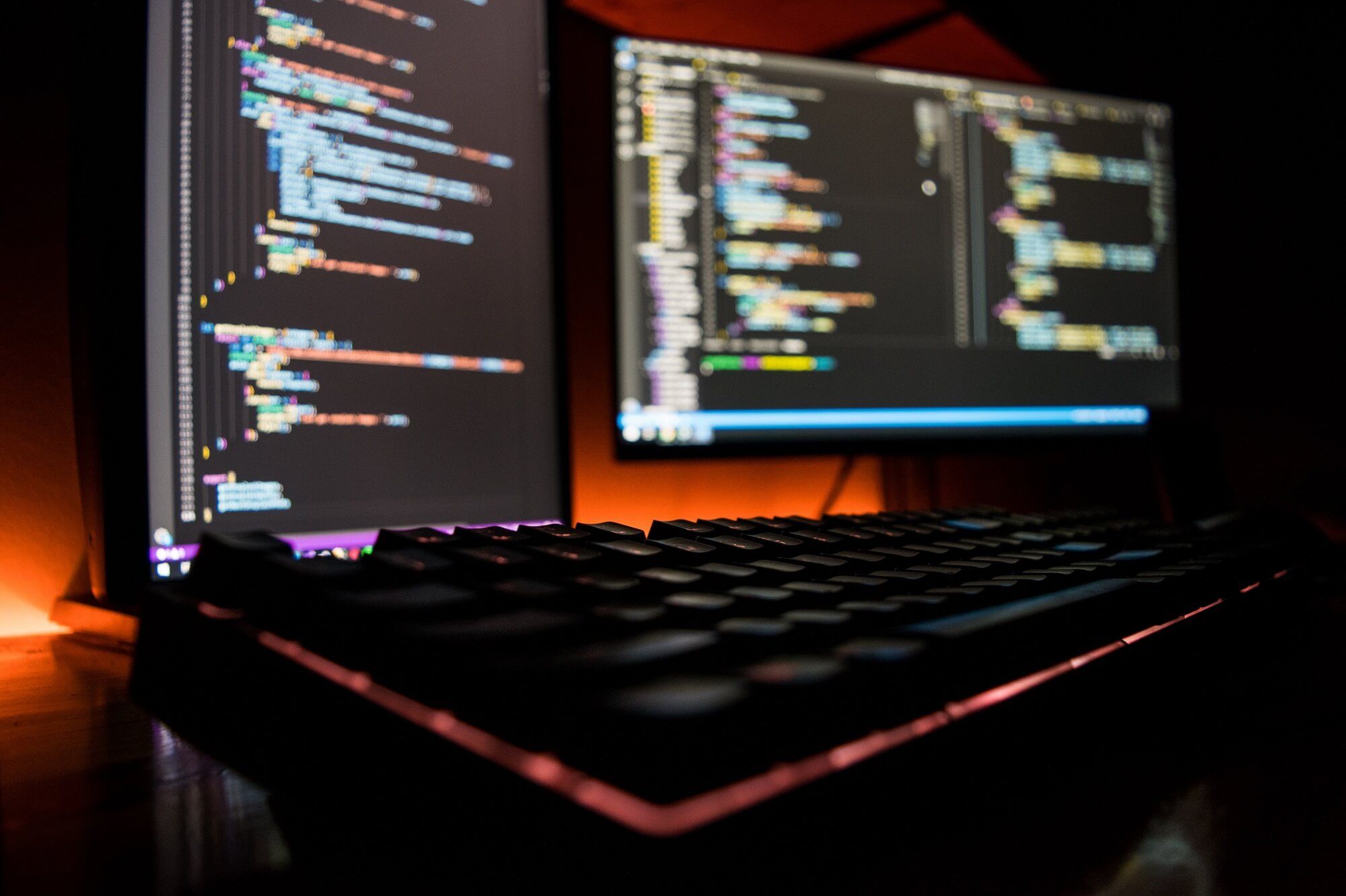 dark room with two pc monitors showing a code editor in the background.